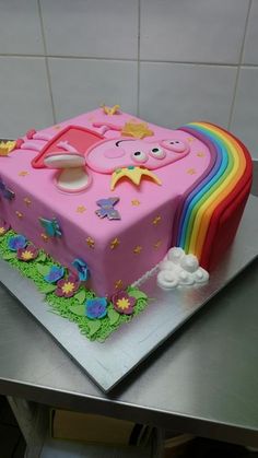 a birthday cake decorated with a pink pig and rainbows on the top is sitting on a table