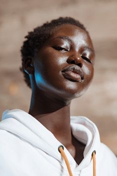 a woman with her eyes closed wearing a white hoodie and orange string around her neck