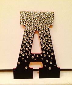 a letter made out of metal rivets on a white wall next to a black frame