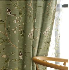 a chair sitting next to a window covered in green floral curtain panels with birds on them