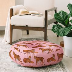 a pink floor pillow with tigers on it next to a chair and potted plant