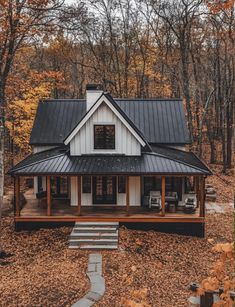 a house in the woods surrounded by trees with leaves on the ground and autumn foliage around it