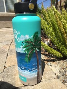 a blue water bottle with a palm tree on the beach painted on it's side