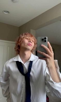 a young man taking a selfie with his cell phone in front of him and wearing a tie