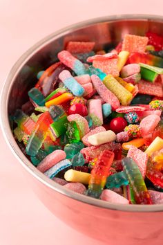 a metal bowl filled with lots of different colored gummy bears on top of a pink surface