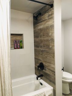 a white bath tub sitting next to a toilet under a wooden paneled bathroom wall