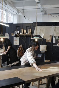 two women are working on wood in an art studio, one is leaning over the table