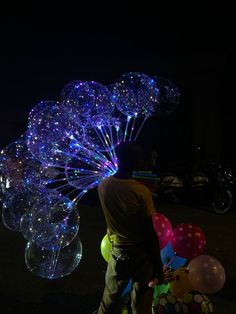 a man is standing next to balloons in the shape of flowers and stars at night