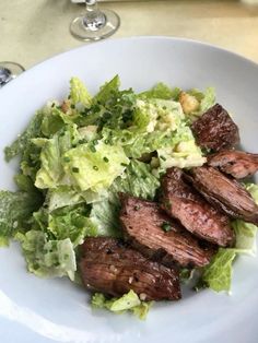 steak and lettuce salad on a white plate with wine glasses in the background