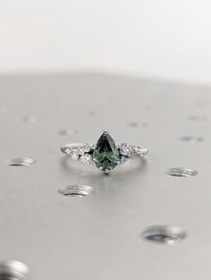 a green diamond ring sitting on top of a silver surface with drops of water around it