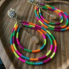 multicolored beaded necklace and earring set on a wooden platter with crystal brooches