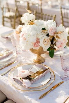 a table set with white and pink flowers in a gold vase on top of it