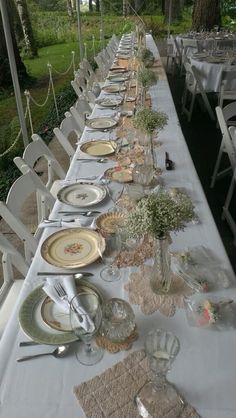 a long table is set up with plates and silverware for an outdoor dinner party