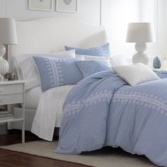 a bed with blue and white comforters in a bedroom next to a lamp on a table