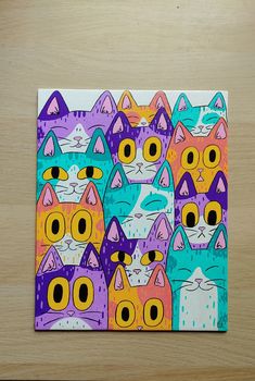 a painting of many cats with different colored eyes and nose shapes, on a wooden surface