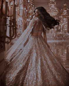 a woman in a gold and white gown with long hair standing near chandelier