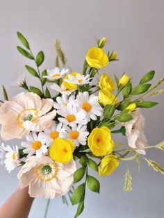 a hand holding a bouquet of flowers with yellow and white blooms in it's center