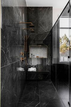 a bathroom with black marble walls and flooring, along with a walk in shower