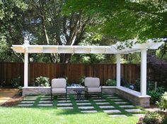 a patio with two chairs and a table under a pergolated trellis on the grass