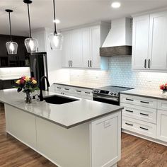 a kitchen with white cabinets and an island in the middle is lit by pendant lights