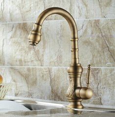 a kitchen faucet that is gold in color with marble wall tiles behind it