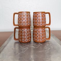 three brown mugs sitting on top of a metal tray with flowers painted on them