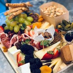 an assortment of cheeses, fruits and crackers on a platter with nuts