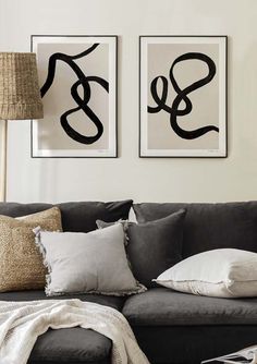 two black and white paintings on the wall above a gray couch in a living room