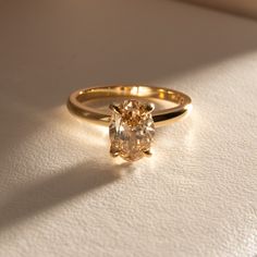 a yellow diamond ring sitting on top of a white table next to a shadow from the sun