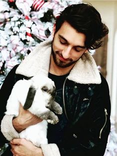 a man holding a baby bunny in front of a christmas tree