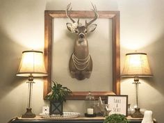 a deer head mounted on the wall above a table with two lamps and other items