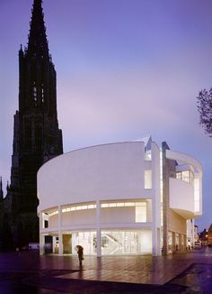 a large white building with a clock tower in the background at dusk, and people walking around it