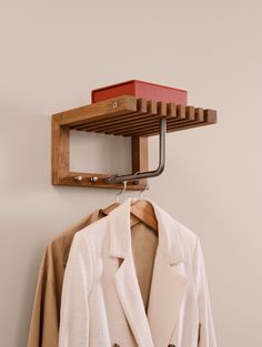 a suit and jacket hang on a clothes rack in front of a white wall with a brown coat hanging from it