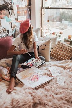 a woman sitting on top of a bed in front of a window reading a book