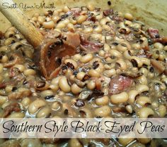 a pot filled with black eyed peas and ham in sauce on top of a wooden spoon