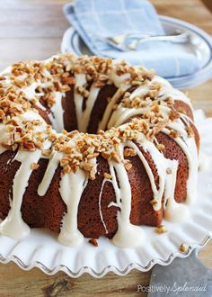 a bundt cake with white icing and nuts on top sitting on a plate