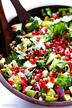 a salad with avocado, pomegranate and feta cheese in a wooden bowl