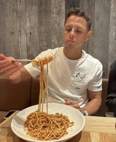 a man sitting at a table in front of a plate of noodles with chopsticks