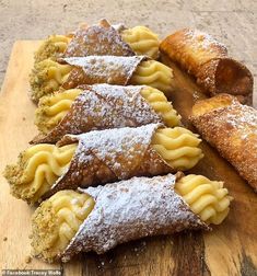 several pastries on a wooden cutting board with powdered sugar and pastry toppings