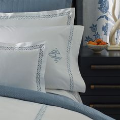 a bed with blue and white sheets, pillows and a bowl of fruit on the nightstand