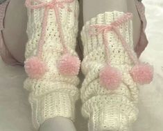 a pair of white crocheted shoes with pink pom - poms on them