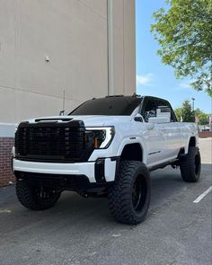 a white truck parked in front of a building with large tires on it's tires