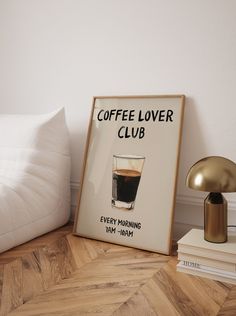 a coffee lover's club poster next to a lamp on a wood floor in a bedroom