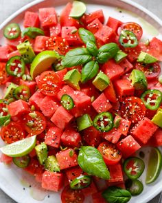 watermelon and basil salad on a white plate with limes, peppers, and tomatoes