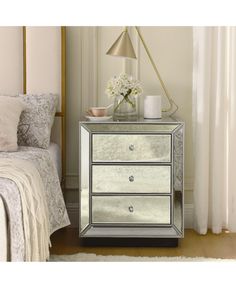 a mirrored chest of drawers in a bedroom with flowers on the nightstand and white bedding