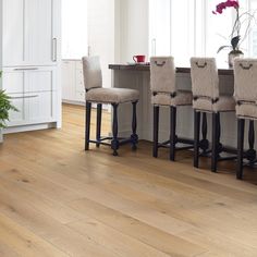 a kitchen with white walls and wooden floors, four stools in front of the counter