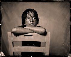 a black and white photo of a boy sitting on a chair with his arms crossed