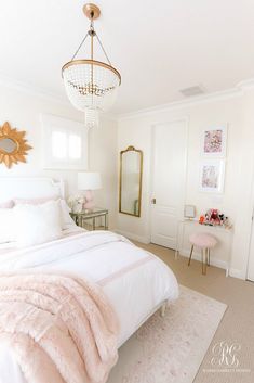 a bedroom with white walls and pink bedding, gold mirror on the wall, and chandelier