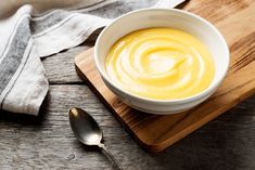 a white bowl filled with yellow sauce on top of a wooden cutting board next to a spoon