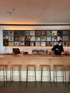 a man in a black jacket behind a bar with stools and bottles on it